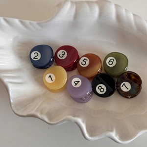 Variety of colorful small acetate hair clips displayed in a white shell-shaped tray