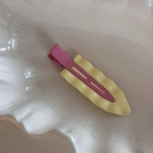 Detail der pastellrosa Metallklammer mit cremegelben Wellenpaneel auf einer Schale