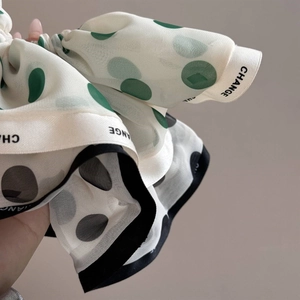 Detail of white chiffon scrunchie with green polka dots and CHANGE lettered edge ribbon