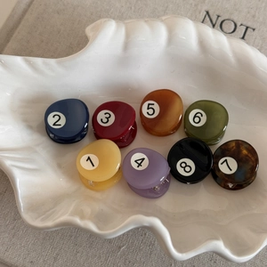 Detail view of eight mini acetate hair clips numbered 1-8 in a white ceramic tray