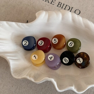 Flat lay of small round acetate hair claws in 8 colors displayed on a shell plate