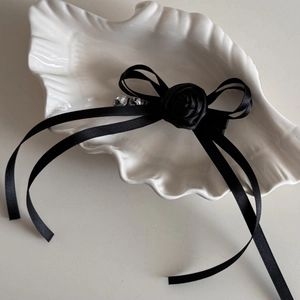 Detail of elegant black satin ribbon bow hair clip with central rose on a shell plate