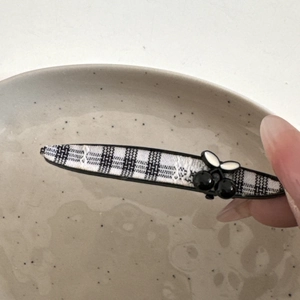 Detailansicht der schwarz-weißen Karo-Haarklammer mit Kirsch-Dekor, in der Hand gehalten