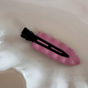 Makro-Detail der wellenförmigen Haarspange mit rosa Finish und schwarzer Metallbasis