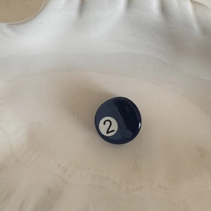 Detail of dark blue pool ball hair clip with number two on white textured background