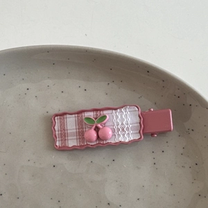 Detail der rosa karierten Haarspange mit Spitzenbesatz und kleinem Kirschanhänger auf Teller