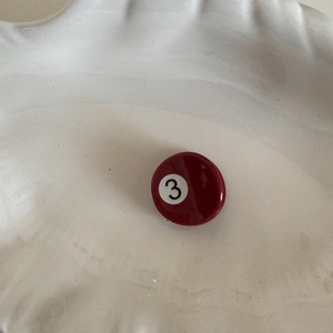 Detail of red billiard number 3 acetate hair claw clip on a white ceramic plate
