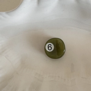 Close-up of olive green billiard ball hair clip with number 6 design on a tray