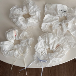 Detailed set of four white lace scrunchies and a pearl bow clip on a soft surface