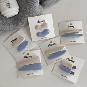Dettaglio di fermagli per capelli in resina opaca blu e beige su carta bianca