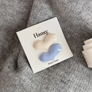 Dettaglio di fermagli per capelli a cuore color crema e celeste su sfondo in maglia morbida