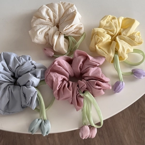 Detail of four colors tulip scrunchies with floral pendants on a white table