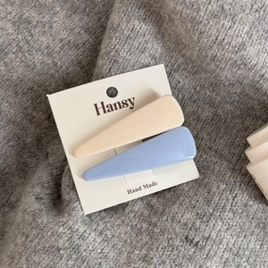 Dettaglio di fermagli per capelli color azzurro e beige su sfondo in maglia grigia