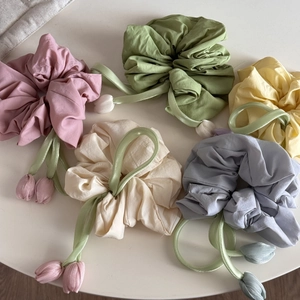 Detail of floral scrunchies with hanging tulip charms in five pastel colors on white desk