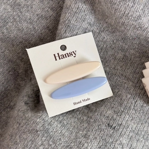 Dettaglio di fermagli per capelli ovali blu pastello e crema su scheda del marchio Hansy