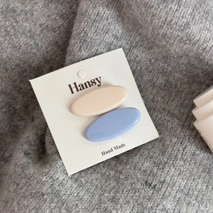 Dettaglio di fermagli per capelli ovali blu e crema su sfondo di maglione grigio morbido