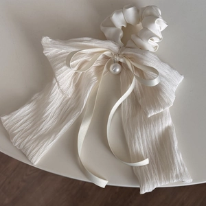 Detail of elegant cream-white layered bow scrunchie with soft satin and pearl drop accent