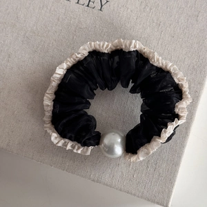Close-up of black mesh scrunchie with white pleated edges and a large faux pearl