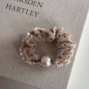 Close-up of beige polka dot mesh scrunchie with ruffle edges and a large white pearl