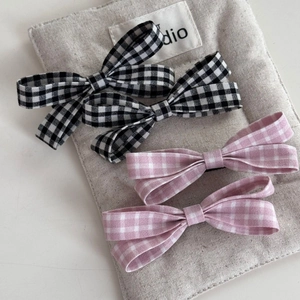 Detailed view of plaid bow hair clips in black and pink on a textured fabric background