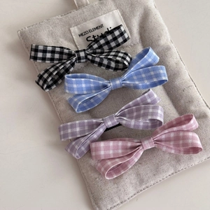 Set of four plaid bow hair clips in black, blue, purple, and pink on a soft gray display pad