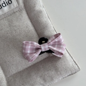 Detailed view of pink plaid bow hair claw clip on soft gray linen fabric texture