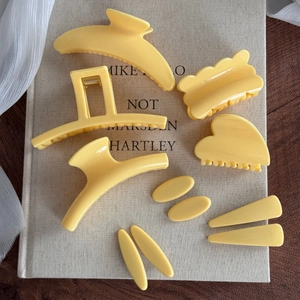 Vue à plat de neuf pinces à cheveux jaune clair mat sur un livre au décor esthétique