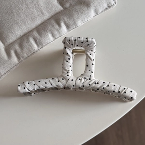 Detailed close-up of large black polka dot fabric hair claw with golden metal spring