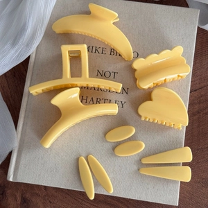 Lot de pinces à cheveux en résine jaune mat aux formes géométriques variées sur livre