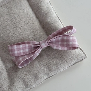 Close-up of pink gingham bow hair clip with fabric texture on a linen display pad