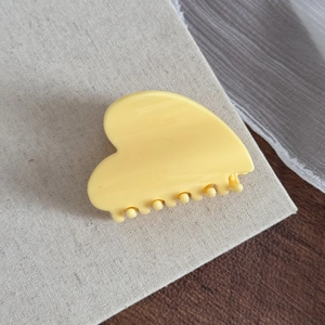 Détail d'une pince à cheveux jaune en forme de cœur sur fond de lin beige