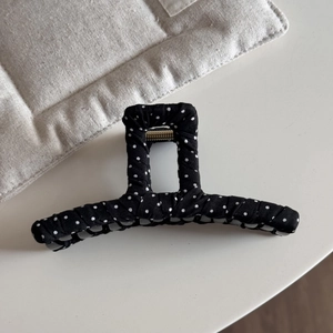 Detail view of a black and white polka dot fabric claw clip with strong metal spring
