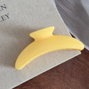 Détail de la pince à cheveux jaune fromage sur tissu beige avec une texture mate élégante