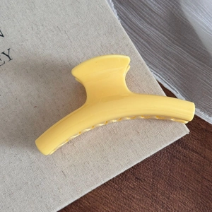 Détail de la grande pince à cheveux jaune brillant sur un fond en tissu beige de style rustique