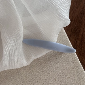 Detail view of a minimalist light blue hair claw clip with a glossy finish on white fabric