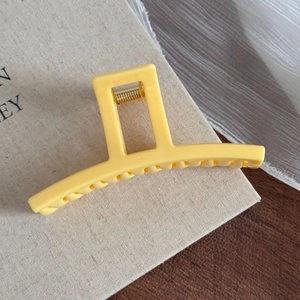 Détail d'une grande pince à cheveux jaune mat avec ressort métallique sur tissu de soie