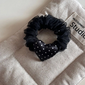 Close-up of black mesh scrunchie with a white polka dot heart charm on linen fabric