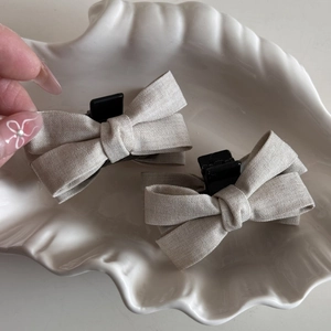 Detail view of beige bow hair clips on a shell tray showing texture and compact size