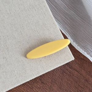 Détail d'une pince à cheveux en résine jaune fromage brillante sur fond lin et bois