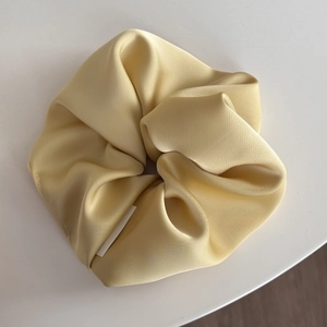 Primo piano dello scrunchie in raso color oro champagne con trama setosa e piccola etichetta