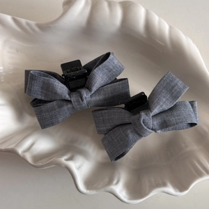 Close-up of two grey linen fabric bow hair clips displayed on a ceramic shell tray