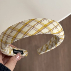 Dettaglio di un cerchietto imbottito a quadri gialli con etichetta tessuta Hand Made