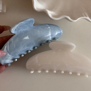 Detail of large hair claws in light blue and cream with marble ink texture patterns