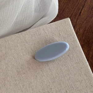 Detail shot of a minimalist light blue oval hair clip on a beige linen display board
