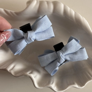 Detail of light blue fabric bow hair clips in a white shell dish for daily styling