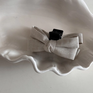 Detail of oatmeal linen bow hair clip showing fabric texture on ceramic tray