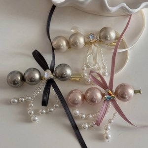 Detail of elegant bow hair clips with pearls and tassels in black, cream, and pink colors