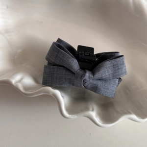 Detailed view of a dark grey bow hair clip with linen texture on a decorative plate