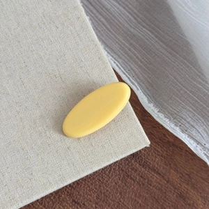 Détail d'une pince à cheveux ovale jaune citron mat en résine sur tissu de lin naturel