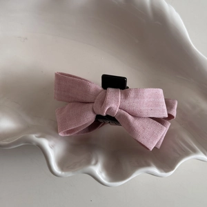 Detailed top view of pink fabric bow hair claw clip on a white shell textured ceramic plate